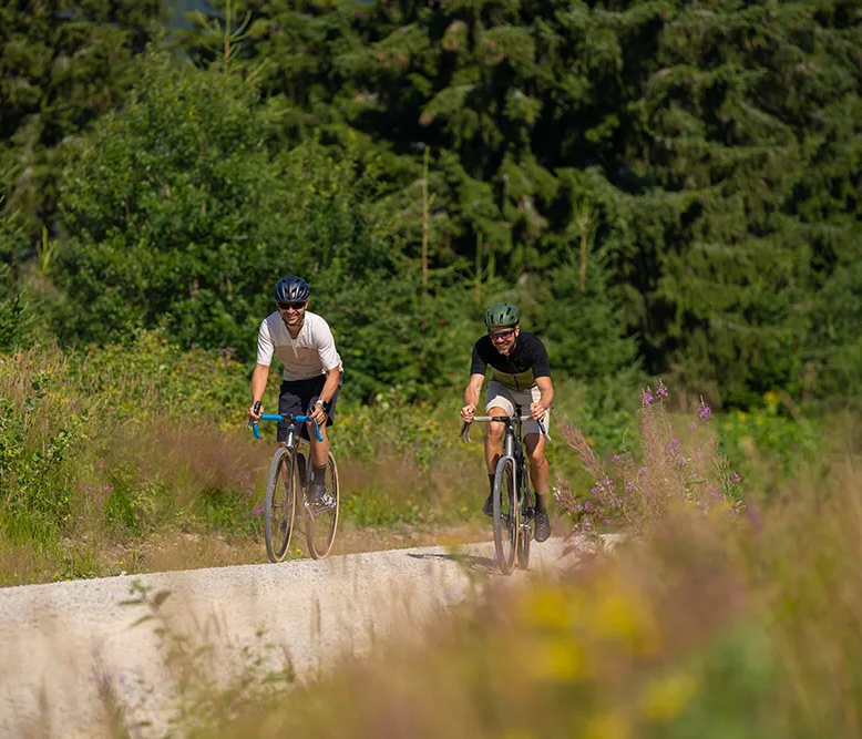 Zwei Radfahrer genießen die Natur auf einem Schotterweg Zwei Radfahrer sind auf einem sonnigen Schotterweg in der Ferienregion Nationalpark Bayerischer Wald unterwegs und erfreuen sich an der üppigen und abwechslungsreichen Natur