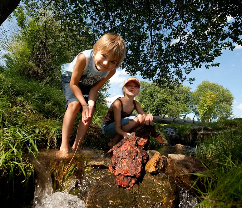 Sommerfreude: Kinder genießen das Plantschen am natürlichen Wasserlauf im Freien Kinder spielen am Bach