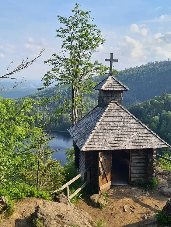 Rachelkapelle mit Rachelsee im Hintergrund Die hölzerne Rachelkapelle thront oberhalb des Eiszeitsees und strahlt Ruhe aus, während sie von Bäumen eingebettet ist und den Blick auf den Rachelsee freigibt.