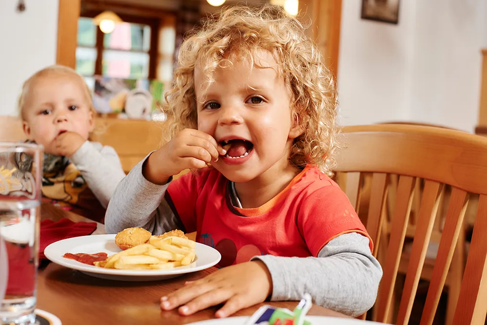 Lächelnde Kinder mit Pommes und Nuggets am Tisch Kinder beim Essen in der regionalen Gastronomie