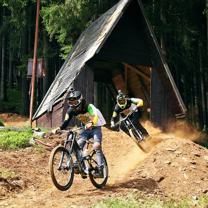2 Mountainbikefahrer meistern den Bikepark in Spicak Zwei Mountainbiker fahren sportlich einen Hang hinunter, das teilweise Staub aufwirbelt