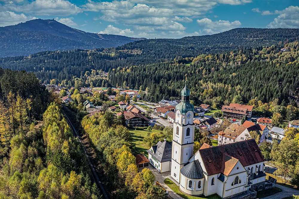 Idyllische Dorfimpression Bayerisch Eisenstein umgeben von majestätischen Bergen Blick auf Bayerisch Eisenstein, im Vordergrund die Kirche, im Hintergrund das Arberareal