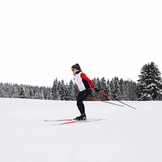 Skilangläuferin beim Skaten in Finsterau Eine sportliche Frau in Skikleidung bewegt sich auf Langlaufskiern elegant über den Schnee, umgeben von einer ruhigen, verschneiten Waldlandschaft.