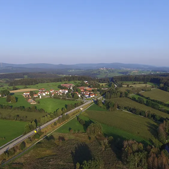 Eine weite Aussicht auf das Örtchen Haslach, umgeben von weiten Wiesenfeldern und Waldflecken, mit dem ruhig gelegenen Hohenauer Naturbadesee, der die natürliche Schönheit noch ergänzt.