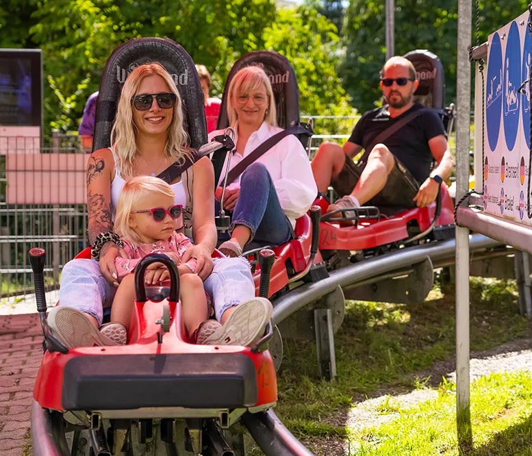 Die Familie lächelt und entspannt sich in ihren Rodeln, während sie auf den Start der Abfahrt des Bärenbob in Grafenau wartet.