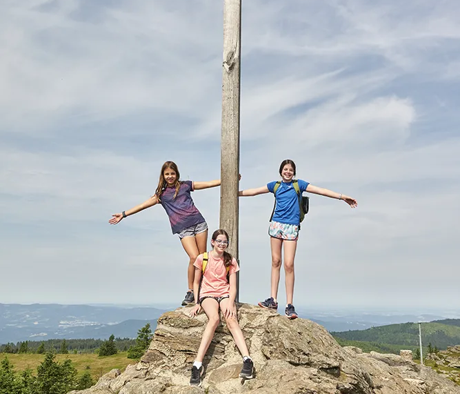 Drei Kinder posieren fröhlich am Gipfelkreuz des Großen Arber Kinder am Gipfelkreuz des Großen Arber