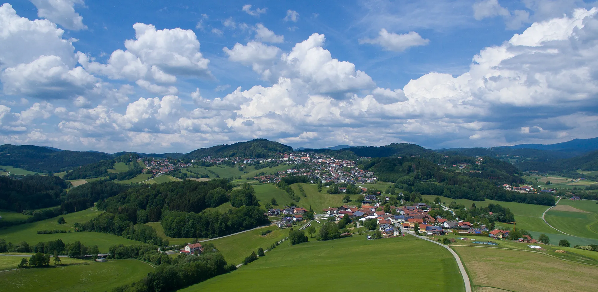 Malerische Landschaft um Schönberg mit sanften Hügeln und Wolken Drohnenblick auf das sogenannte Meran des Bayerischen Waldes, umrahmt von hellgrünen Wiesen und bewaldeten Waldwogen
