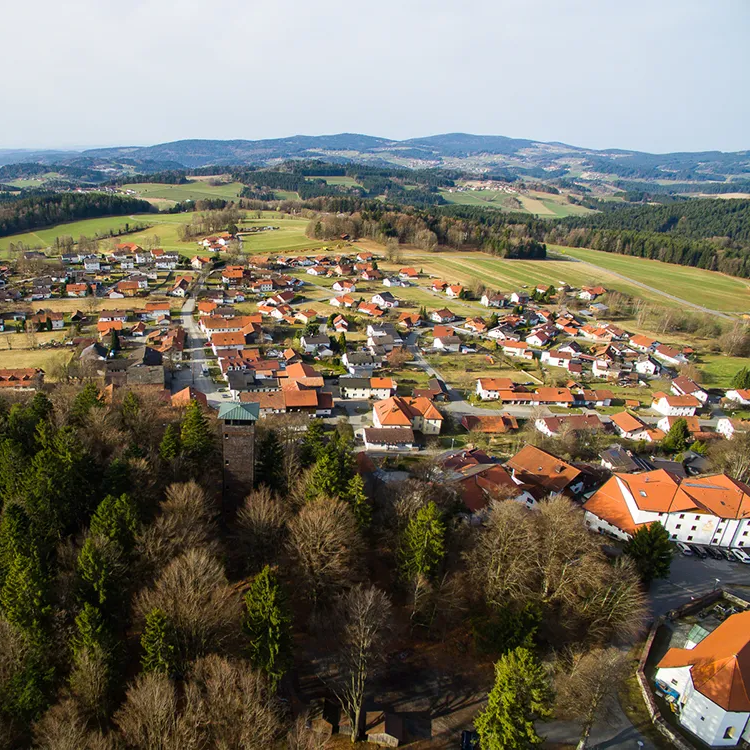 Ein luftiger Blick auf das Oberkreuzberg, das dicht am Wald liegt, mit landwirtschaftlichen Flächen und Hügelland rundum.