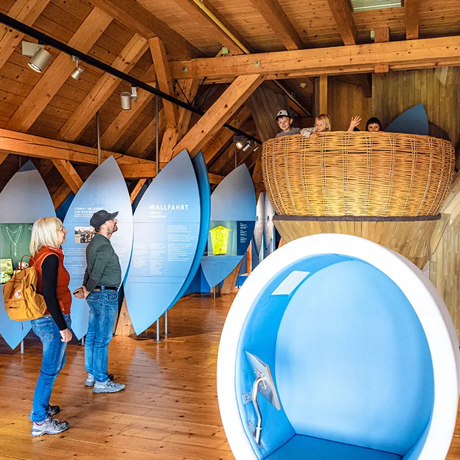 Besucher auf Entdeckertour im Nationalparkmuseum Zwei Besucher betrachten das Nest des begehbaren Baums im Waldgeschichtlichen Museum, während Kinder erfreut herausschauen.