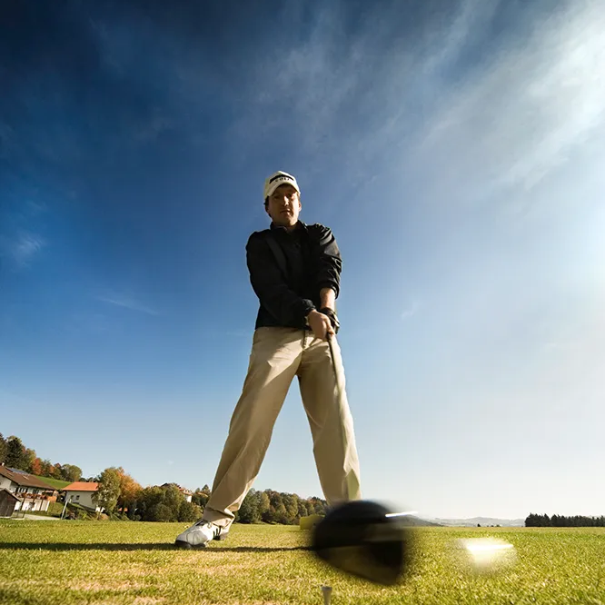 Ein Golfer in sportlicher Kleidung bereitet sich auf einen Abschlag auf dem sonnigen Golfplatz vor.