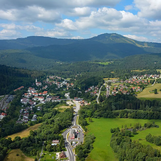 Ein Blick auf das wunderschön in die Grenzregion eingebettete Bayerisch Eisenstein, mit dem Grenzbahnhof in Sicht, dem Großen Arber im Hintergrund und Wolken am Himmel.