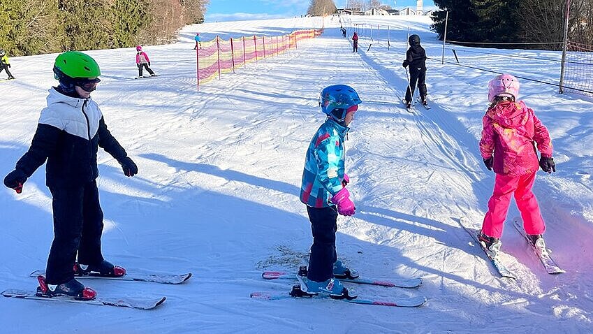 Kinder mit Skiern und Schneeanzug warten auf der Skipiste Kinder am Skilift