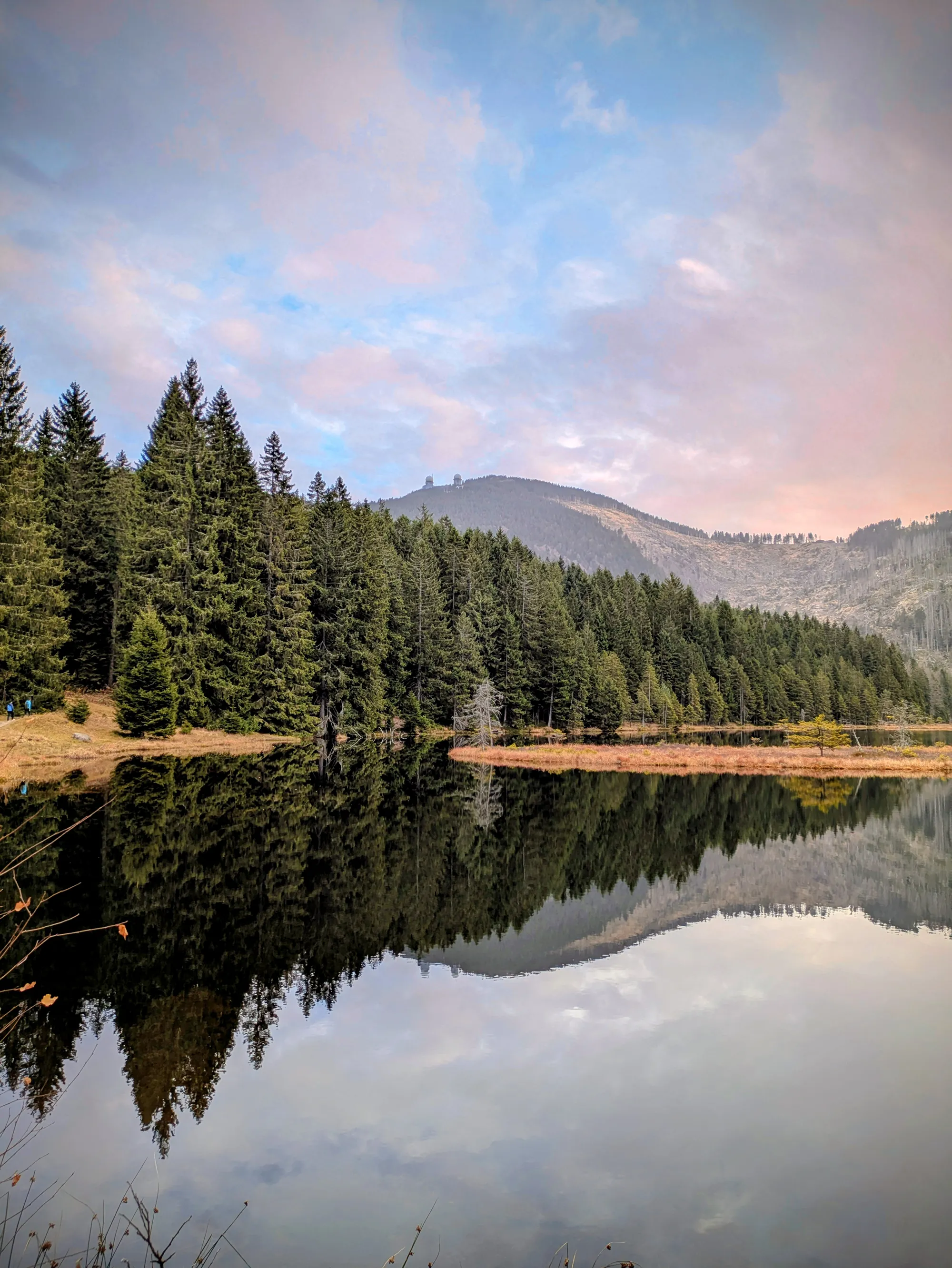 Der Kleine Arbersee mit dahinterliegendem Wald und Bergen, die sich im Abendrot im Wasser spiegeln.