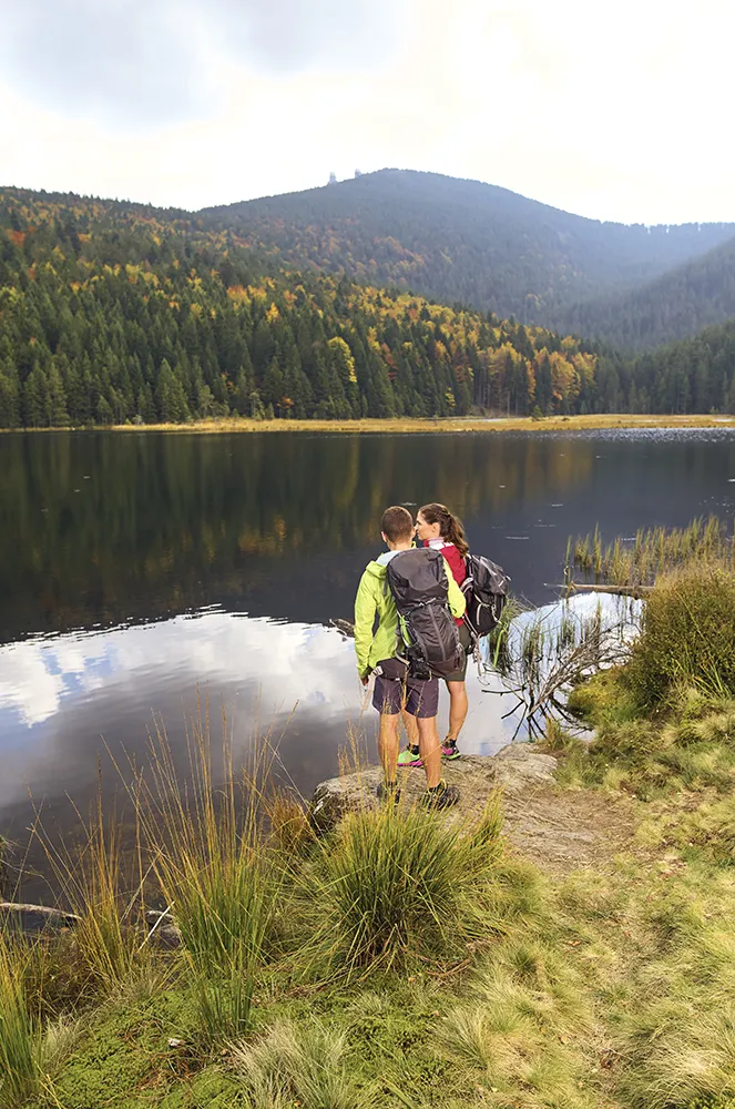 Ein junges Pärchen steht mit Rucksack und Wandersachen vor dem Arbersee Zwei Wanderer blicken auf den Arbersee
